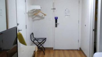 Una habitación pequeña y funcional con suelo de madera, un escritorio con computadora, una silla, una cama y una puerta con cerradura.