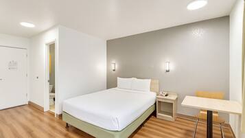 Una habitación de hotel con cama, mesita de noche, sillón y un escritorio pequeño con silla.