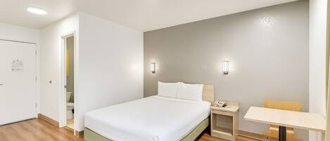 A hotel room with a bed, bedside table, chair, and a small desk with a chair.