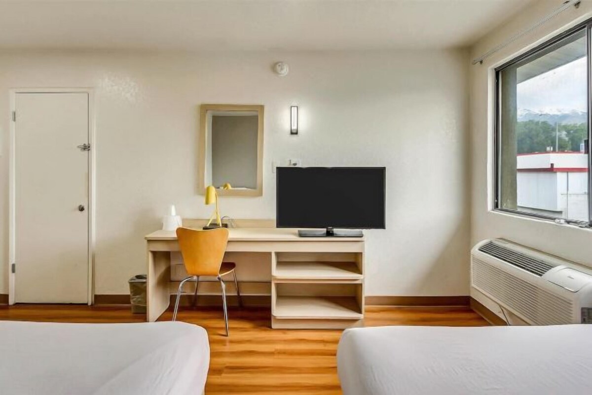 A hotel room with a bed, a desk with a chair, a TV, and a window with a view of mountains.