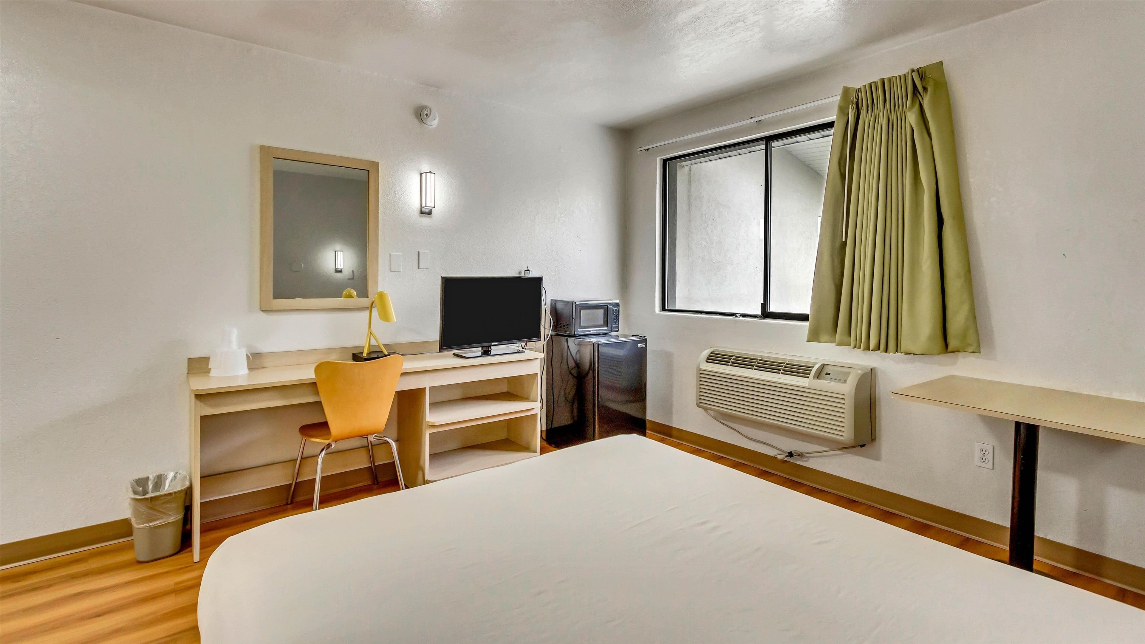 A hotel room with a bed, desk, chair, TV, microwave, and window with curtains.