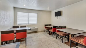 Una sala de conferencias con una mesa grande, varias sillas, un televisor de pantalla plana y un ventanal con persianas.
