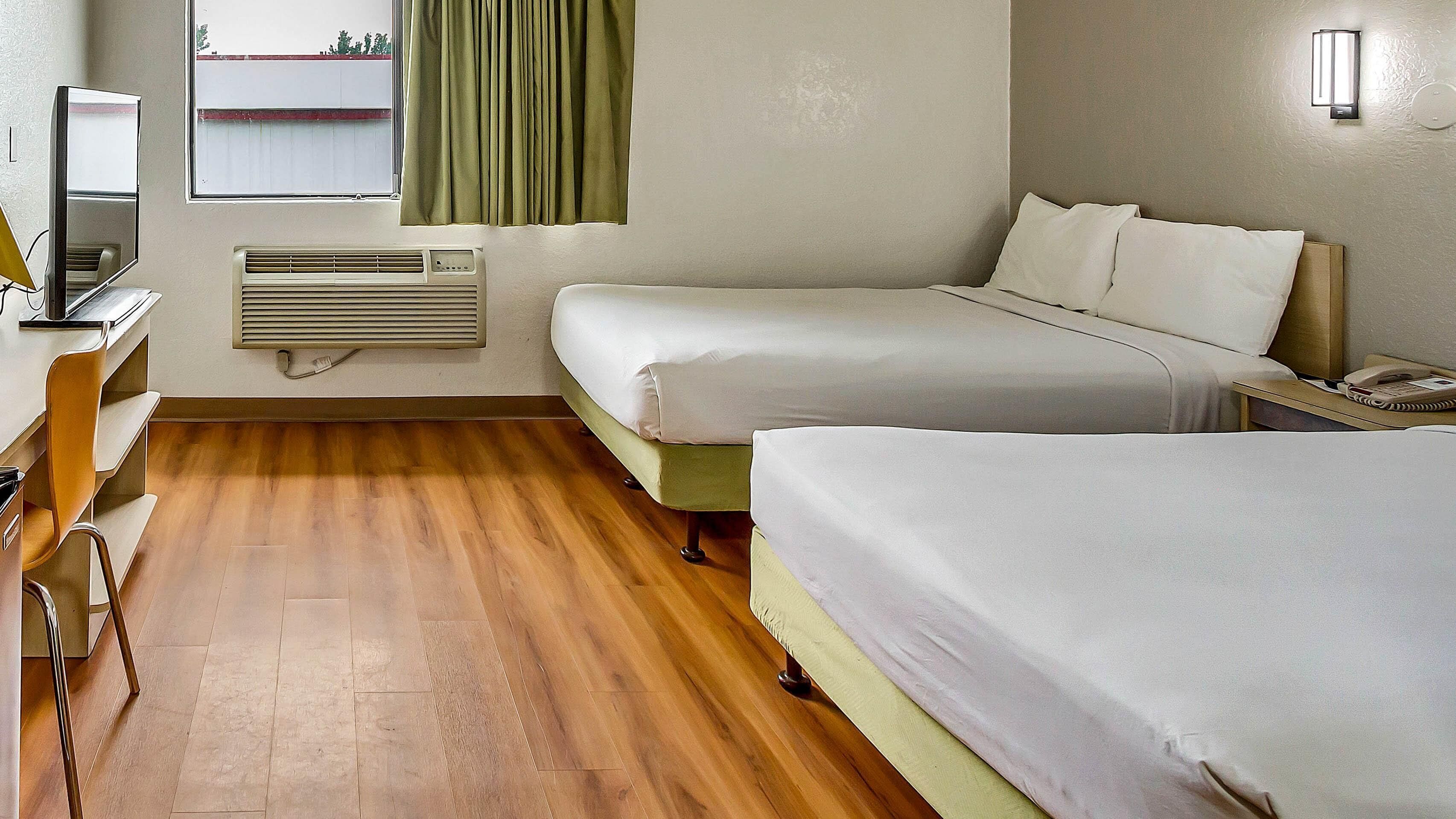 Une chambre d’hôtel avec deux lits, un bureau avec une chaise, une télévision et une fenêtre avec des rideaux.