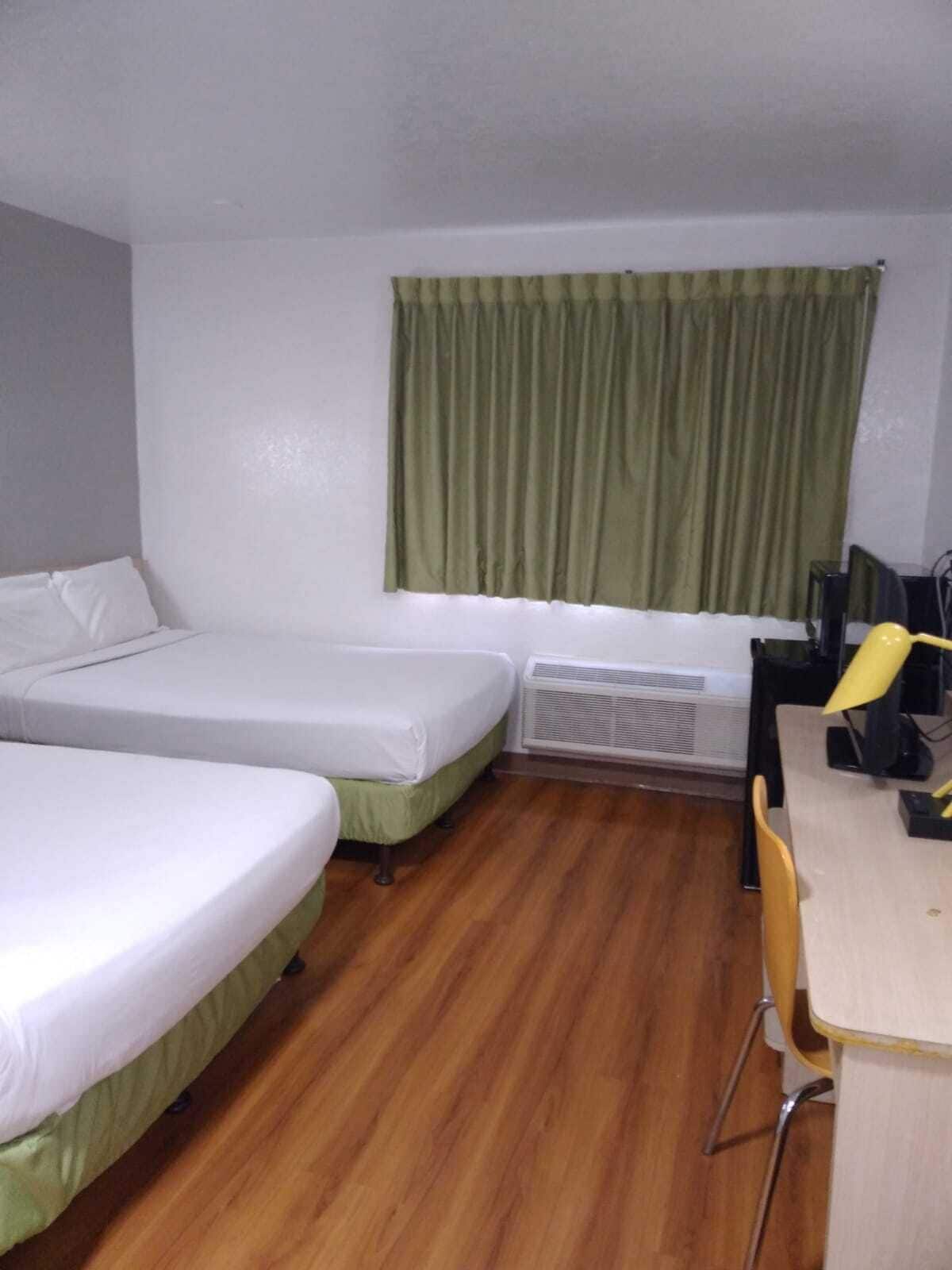A small, clean room with two single beds, a desk with a chair, and a window with green curtains.