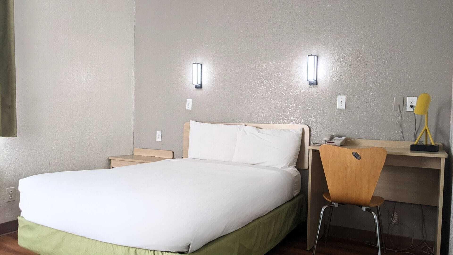 A hotel room with a bed, a desk, and two wall-mounted lights.