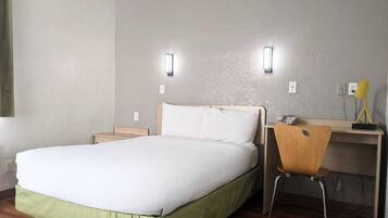 A hotel room with a bed, a desk, and two wall-mounted lights.