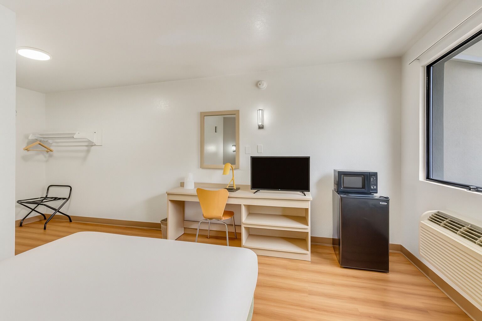 Una habitación de hotel con cama, escritorio, computadora, silla, televisor y calefactor.