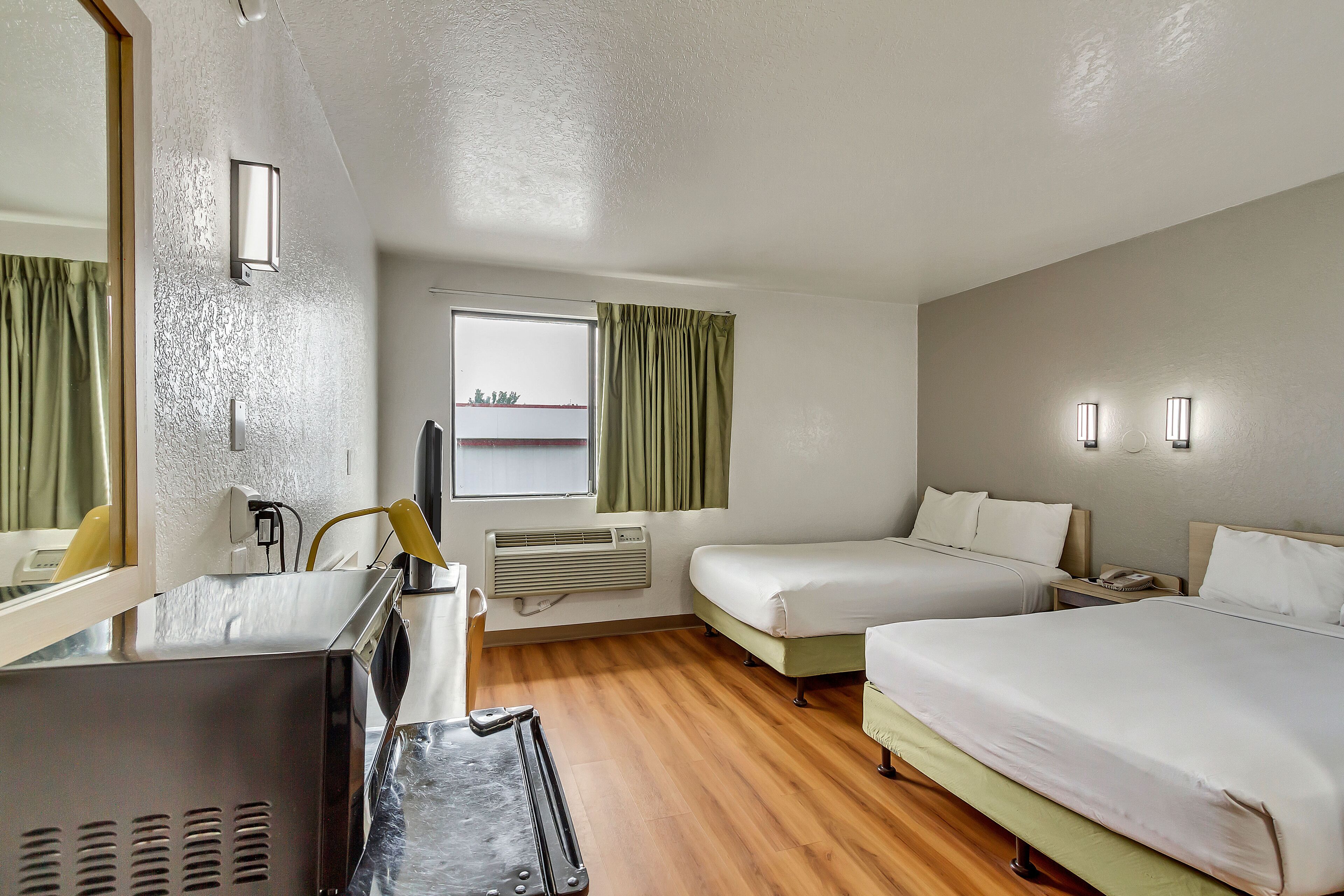 A hotel room with two beds, a desk with a computer, a mirror, and a window with curtains.