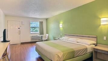 A hotel room with a bed, a desk, a chair, and a window.