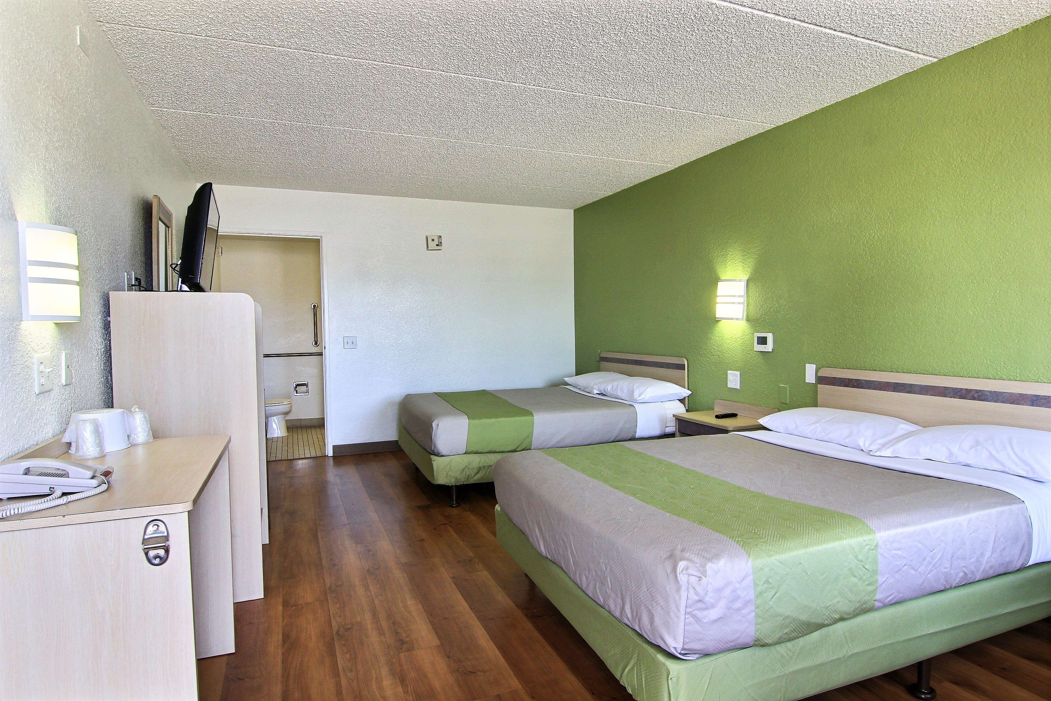 Habitación de hotel con dos camas, un escritorio, un espejo y un baño visible al fondo.