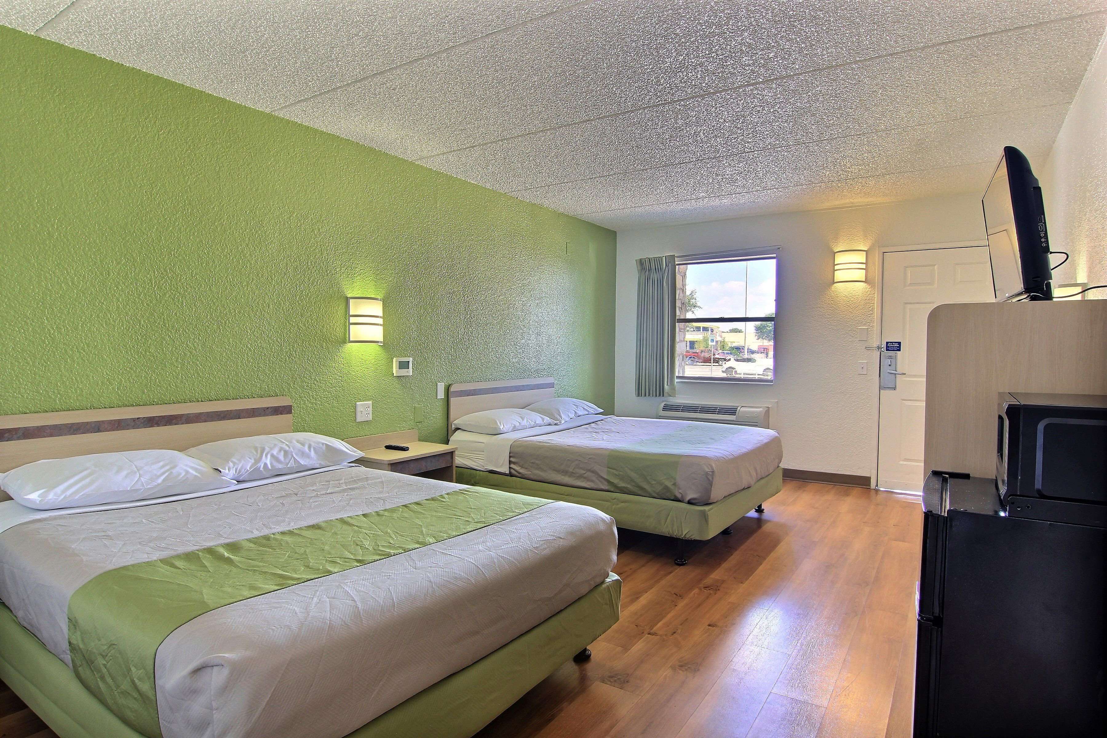 Une chambre d’hôtel avec deux lits, un bureau, un réfrigérateur et une fenêtre donnant sur l’extérieur.
