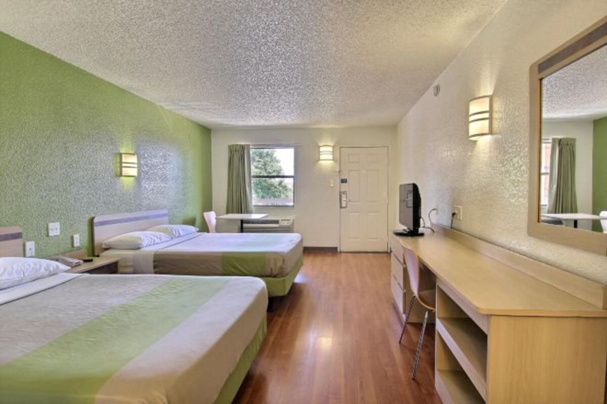 A hotel room with two beds, a desk, a mirror, a TV, and a window with curtains.