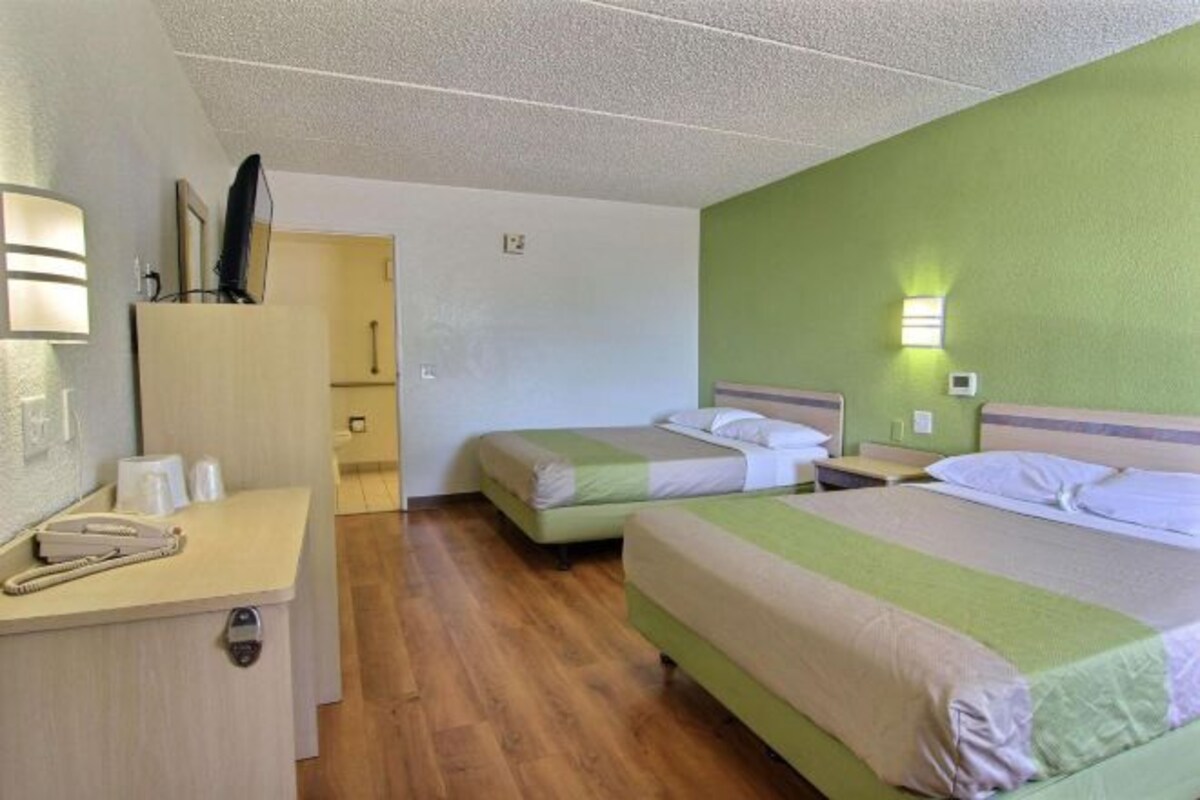 A hotel room with two beds, a desk with a telephone, and a green wall.