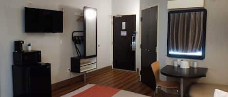 Una habitación de hotel con cama, escritorio con computadora, televisor, espejo y puerta.