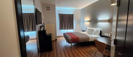 A hotel room with a bed, bedside table, chair, desk, and wardrobe.
