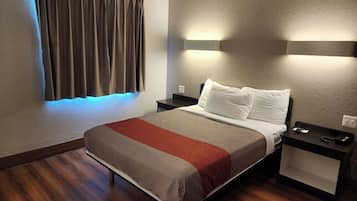 A hotel room with a bed, bedside tables, a nightstand, a window with curtains, and wall-mounted lighting.