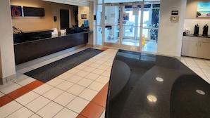 A modern lobby with a reception desk, a coffee station, and a glass door entrance. - Motel 6 Biloxi, MS - Beach (Biloxi)