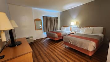 A hotel room with two beds, a desk, a lamp, a mirror, and a window with curtains.