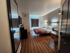 Una habitación de hotel con cama, mesita de noche, silla, escritorio y televisor.