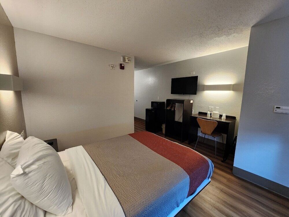 Une chambre d’hôtel équipée d’un lit, d’un bureau, d’une chaise, d’une télévision et d’une petite kitchenette.