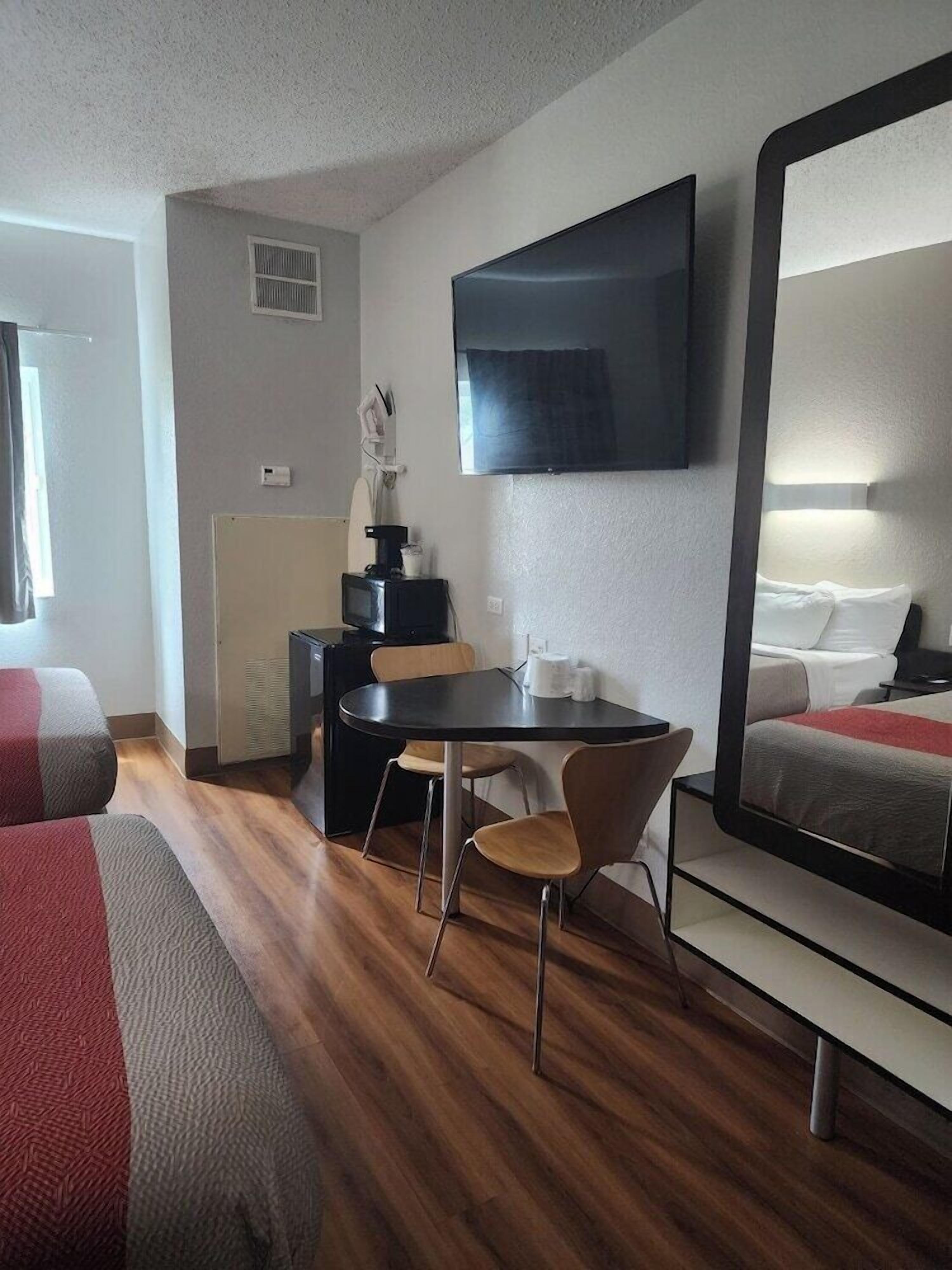 Une chambre d’hôtel comprenant un lit, un bureau avec une chaise, un téléviseur fixé au mur et un grand miroir.
