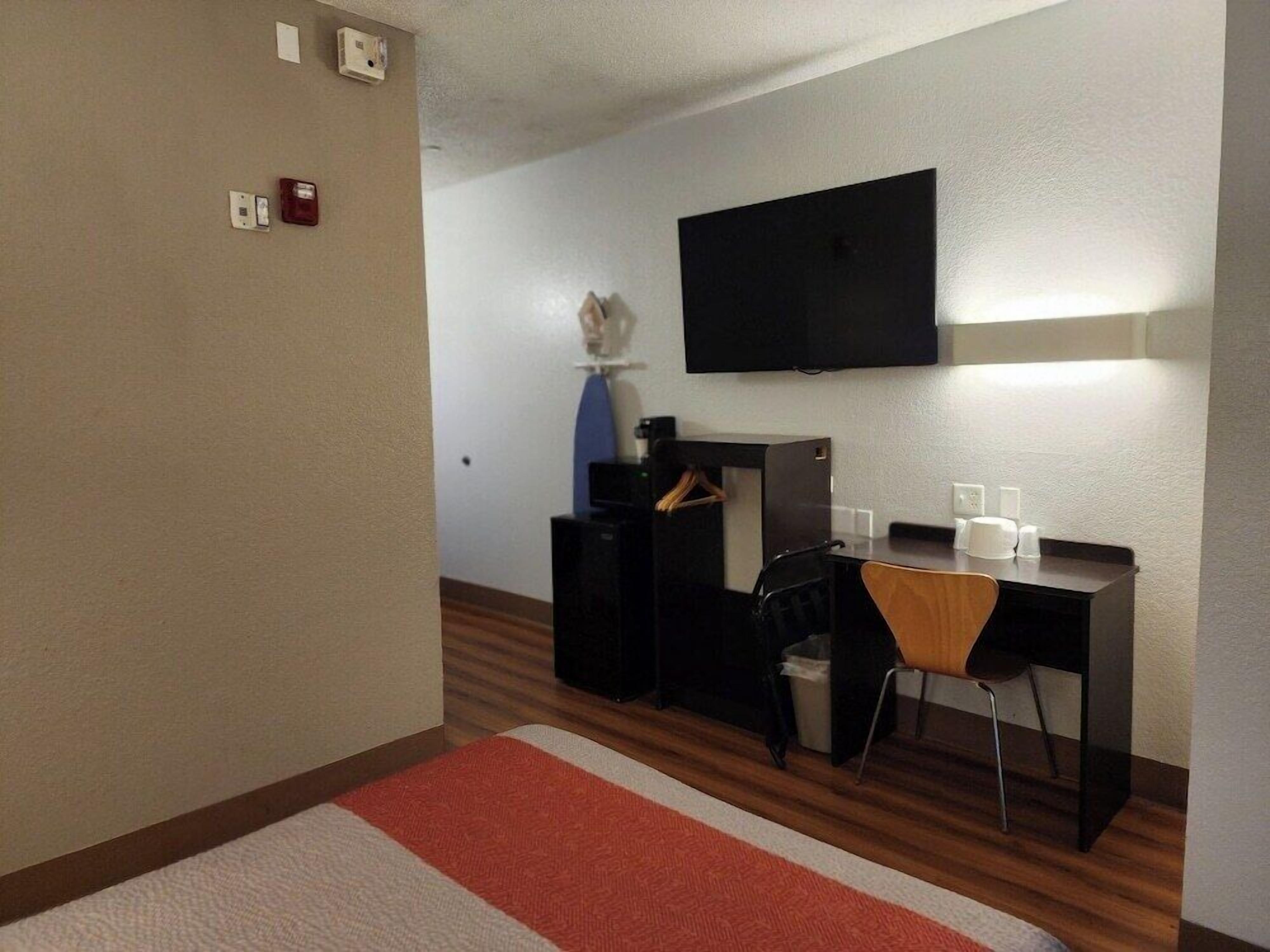 A hotel room with a bed, a desk, a chair, a television, and a small table with toiletries.