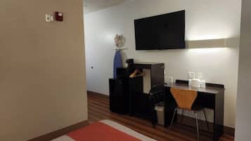 A hotel room with a bed, a desk, a chair, a television, and a small table with toiletries.
