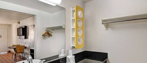 Un baño moderno con encimera negra, lavamanos blanco, espejo y toallero amarillo.