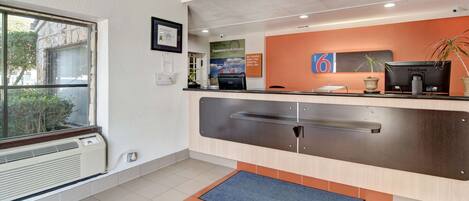 Zona de recepción con ventanal, mostrador, monitor ViewSonic, planta y un certificado enmarcado en la pared.