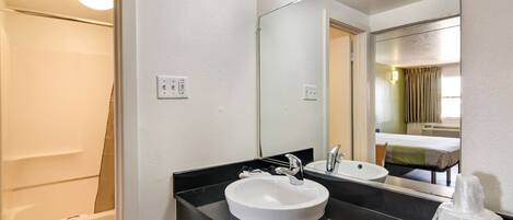 A hotel bathroom with a white sink, black countertop, and a large mirror.
