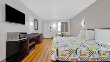 Una habitación de hotel con cama, escritorio con computadora, televisor en la pared y una kitchenette pequeña.