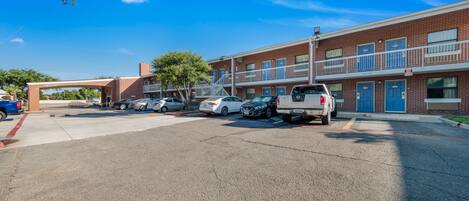 Un estacionamiento con varios coches y un edificio de múltiples puertas y ventanas.