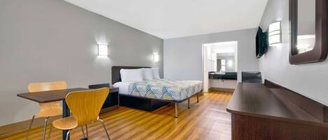 Una habitación de hotel moderna con suelo de madera, cama con ropa de cama estampada, escritorio con silla y un espejo grande en la pared.