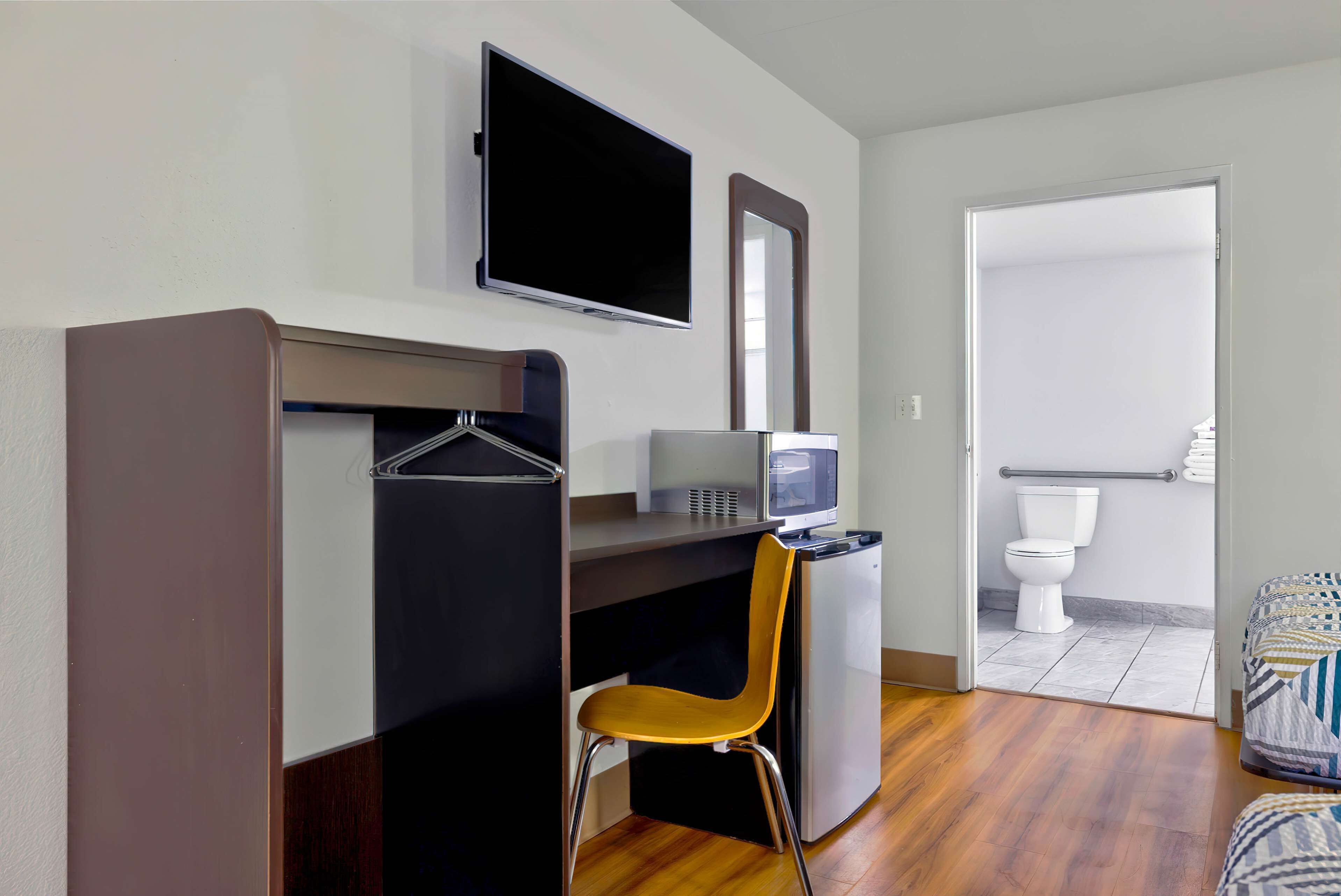 Habitació d'hotel compacta amb escriptori, cadira, televisió i petita cuina.