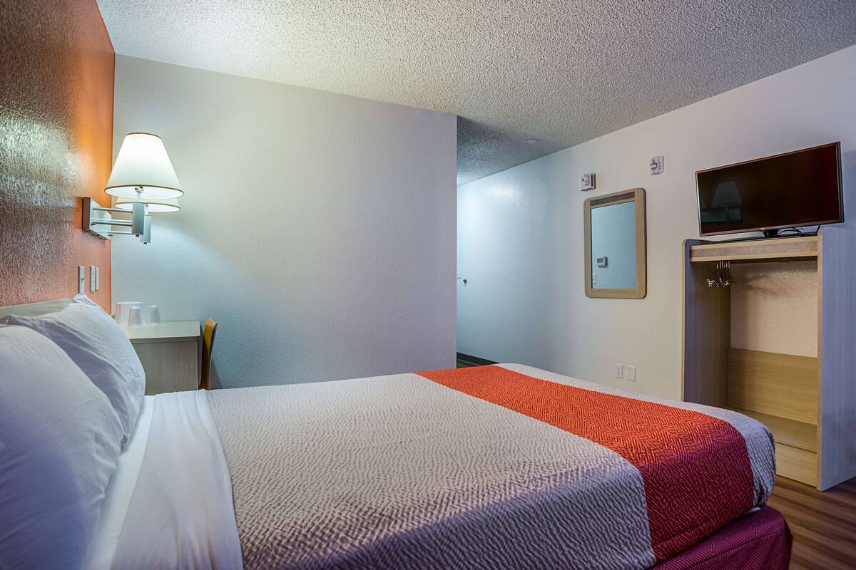 Una habitación de hotel con cama, escritorio, televisor y armario.