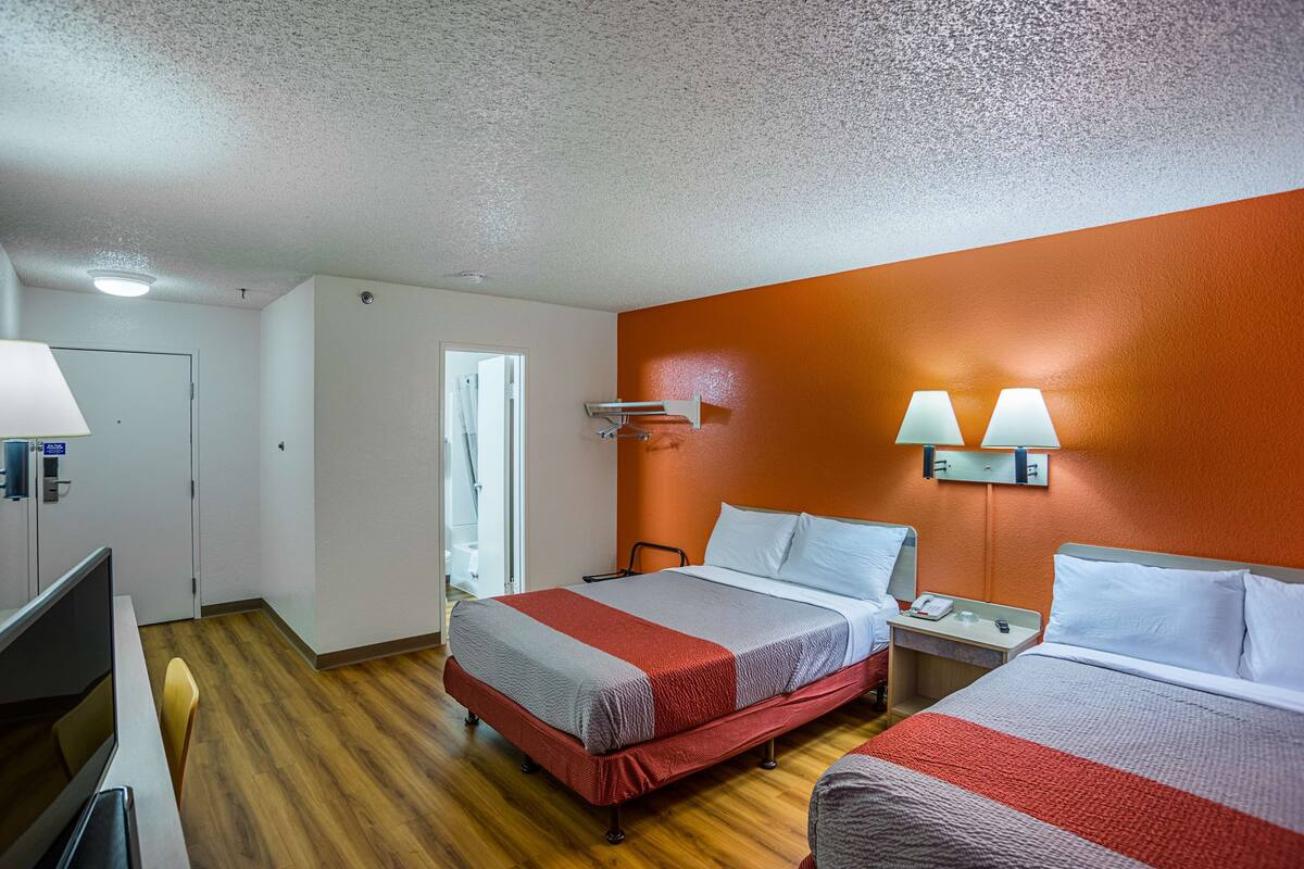 Habitación de hotel con dos camas, un escritorio, una silla, un televisor y la puerta del baño.
