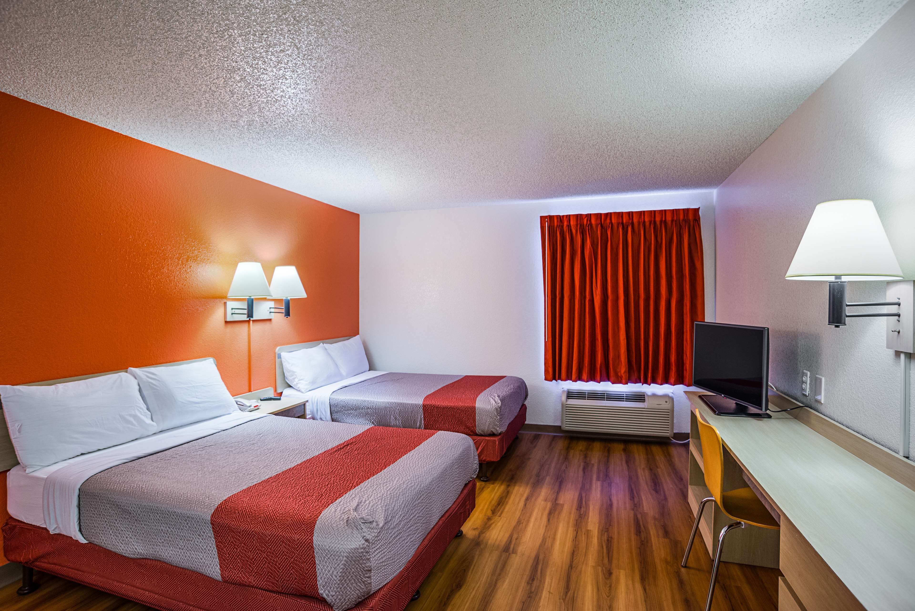 A hotel room with two beds, a desk with a computer, a TV, and a window with curtains.