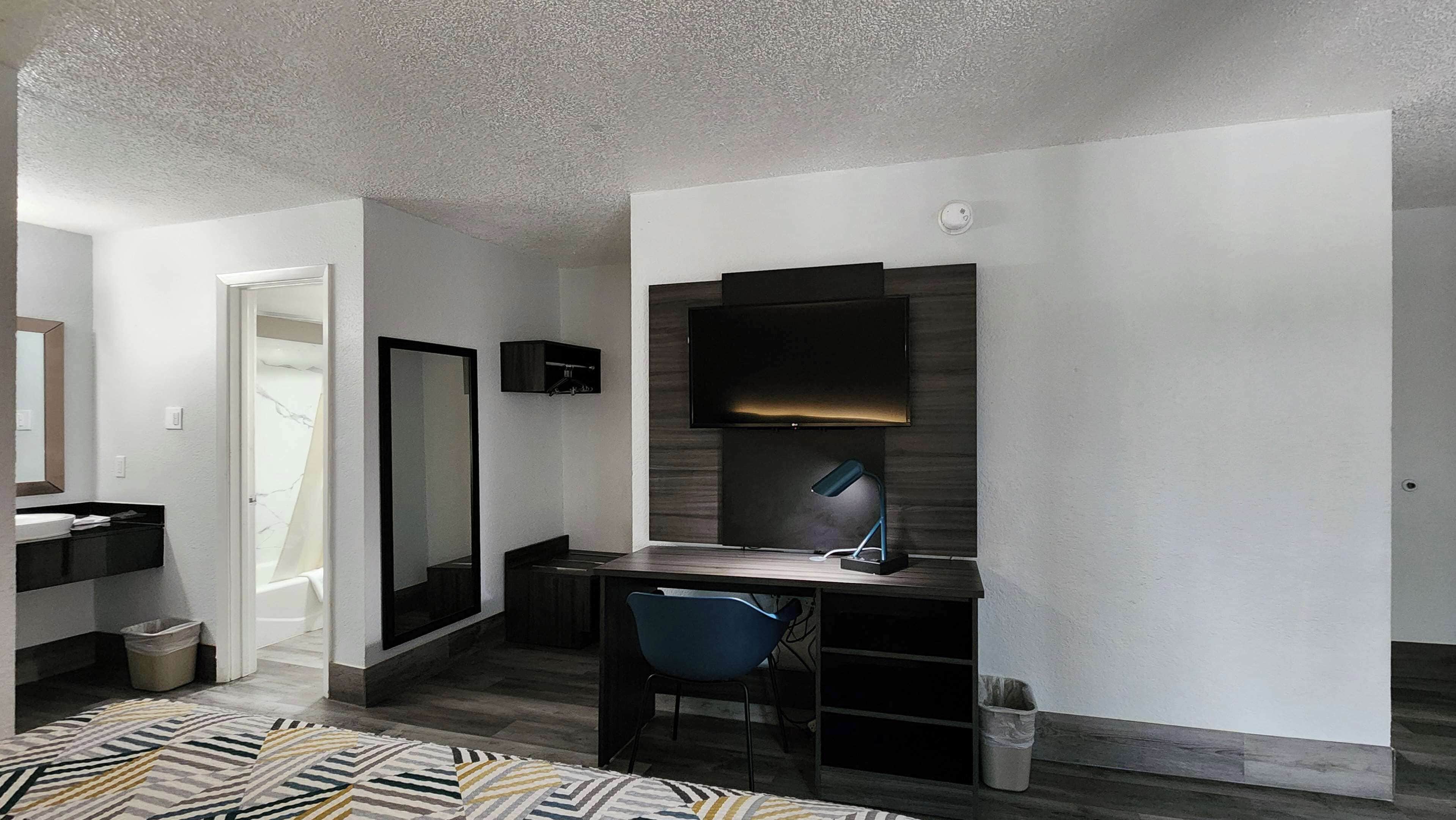 A modern bedroom with a bed, a desk with a chair, a TV, and a mirror.