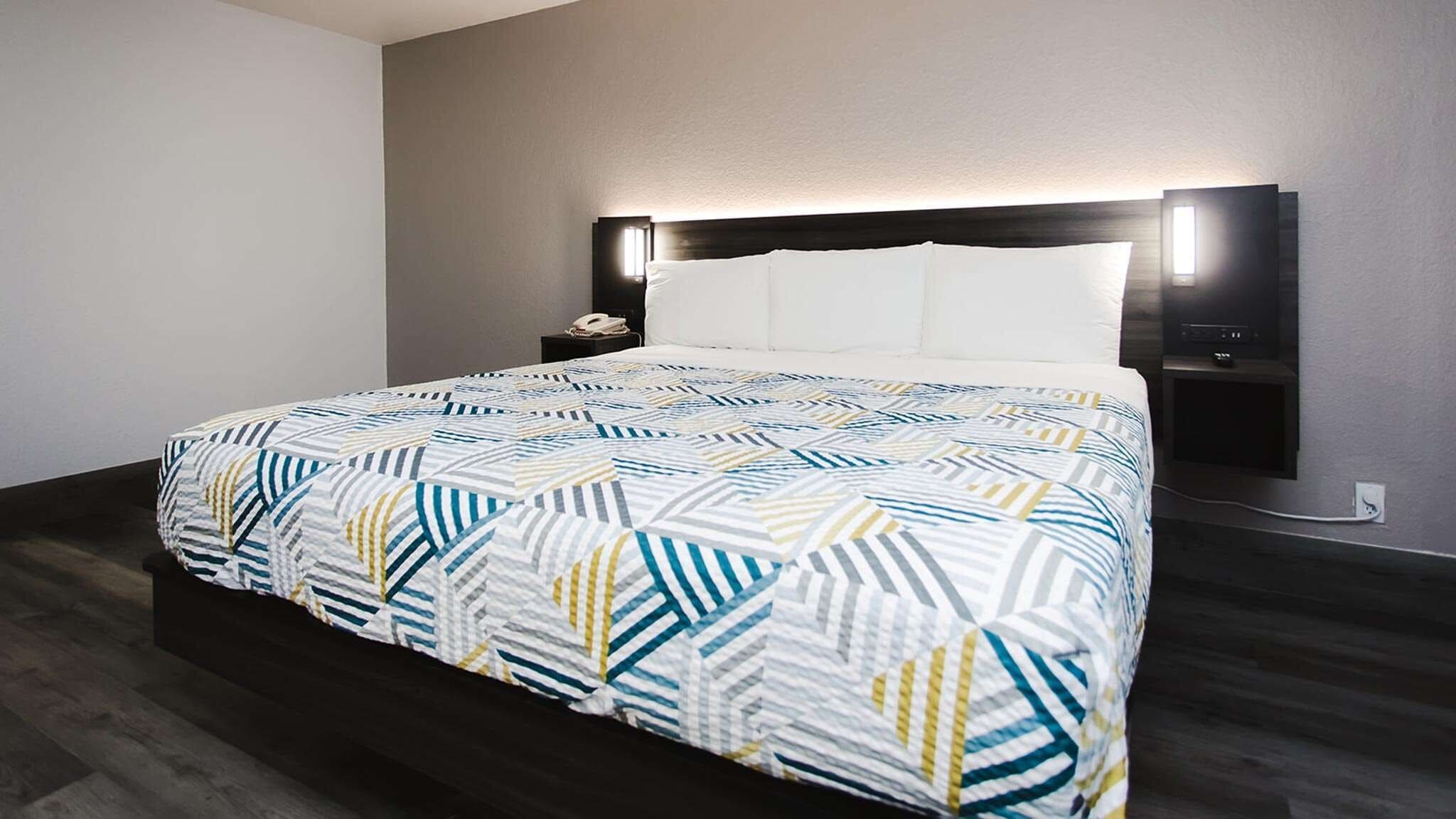 Une chambre d’hôtel moderne avec un grand lit, une table de chevet et un téléviseur fixé au mur.