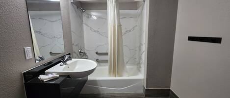 A bathroom with a white sink, a mirror, a shower with a curtain, and a marble wall.
