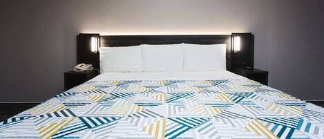 A neatly made bed with a geometric patterned bedspread, a dark headboard with integrated lighting, and a bedside table with a phone and a small decorative item.