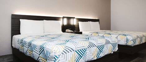 A hotel room with two beds, each with a patterned bedspread and white pillows. There is a nightstand with a phone and a lamp between the beds.