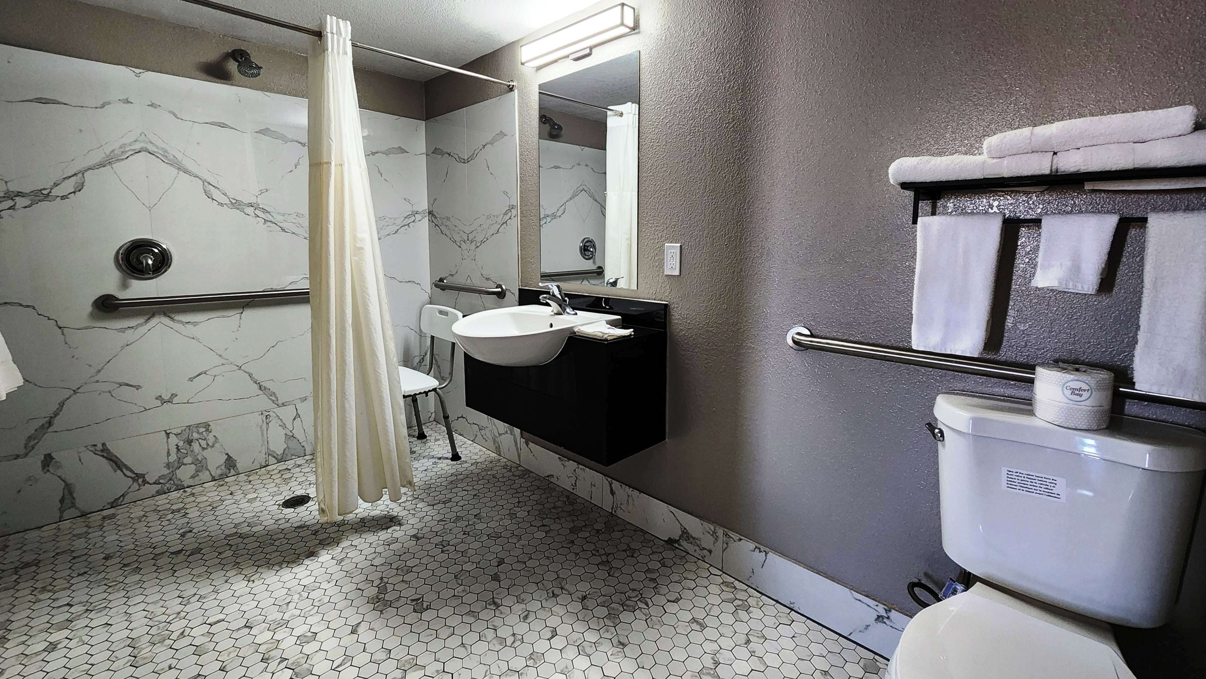 A bathroom with a hexagonal tile floor, a white sink, a black vanity, a mirror, a shower with a curtain, and a toilet.