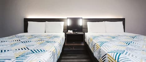 Habitación de hotel con dos camas, cada una con ropa de cama estampada, una mesita de noche con lámpara y un aplique en la pared.