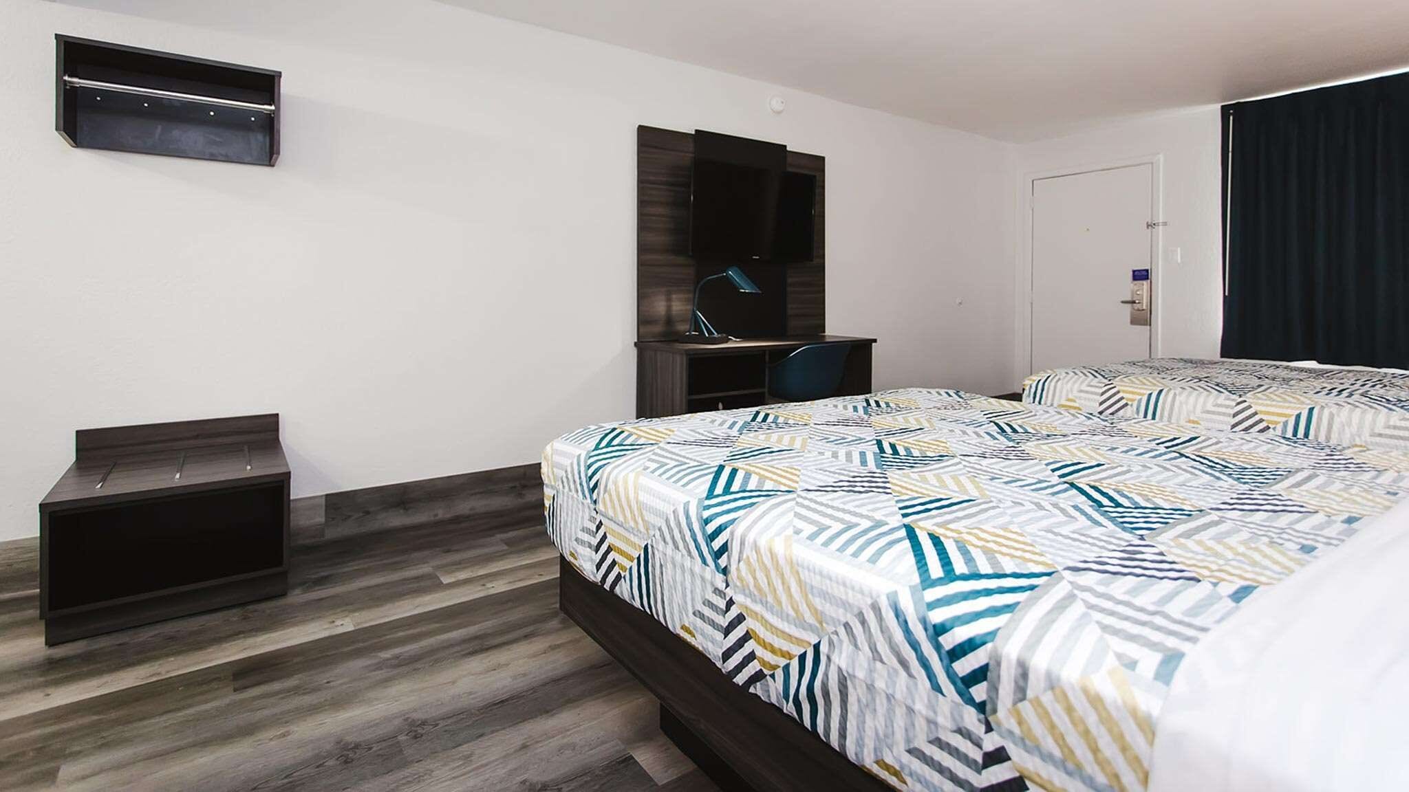 Une chambre d’hôtel moderne équipée d’un lit, d’un bureau, d’une chaise, d’une télévision et d’une armoire.