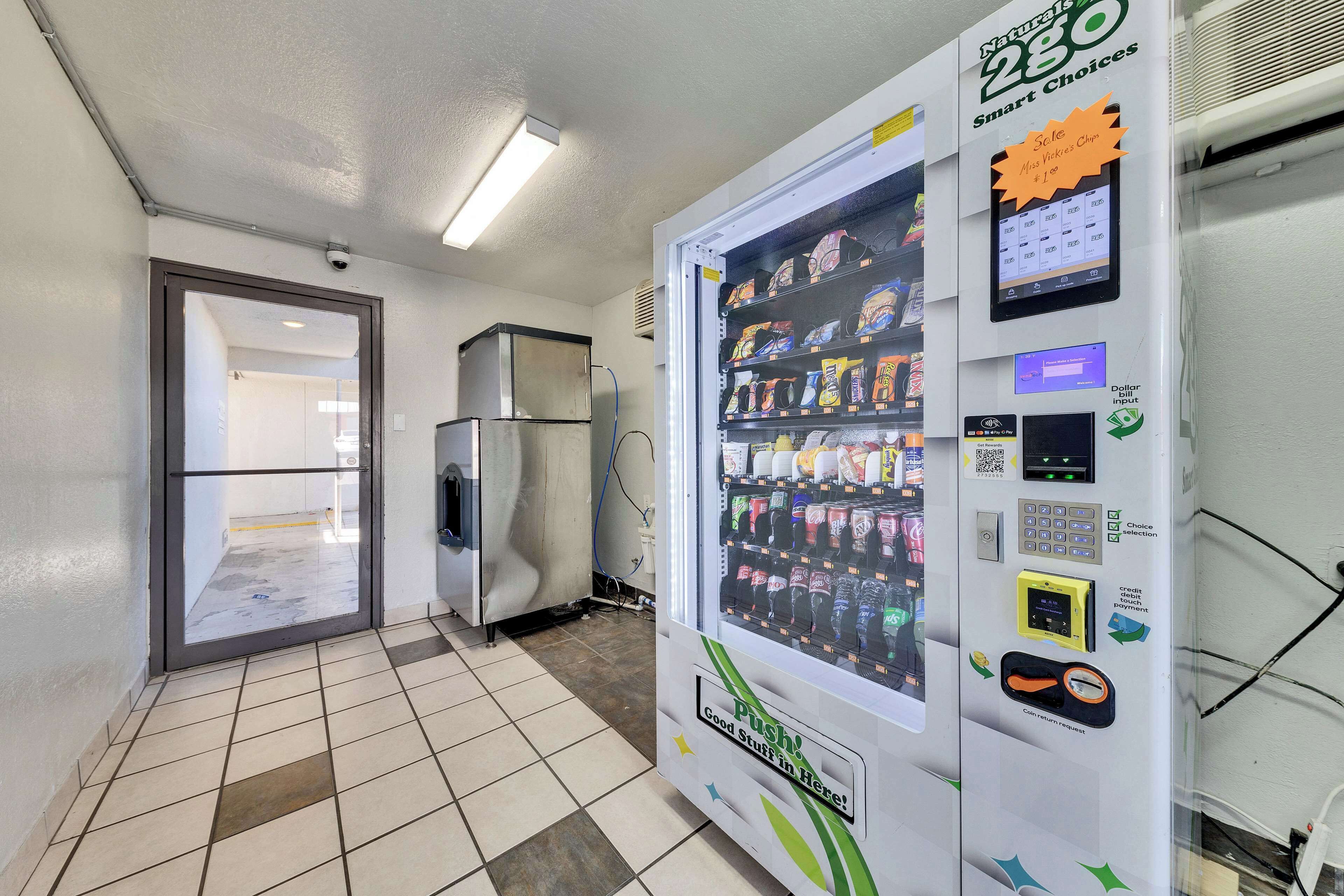 Ein Getränkeautomat mit verschiedenen Snacks und Getränken, einem digitalen Bezahlschirm und einer Taste zum Ausgeben der Artikel.