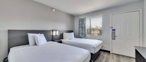 Een hotelkamer met twee bedden, een raam met behang gordijnen, een deur en een klein bureau.