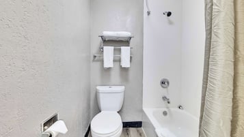 Une salle de bain comprenant des toilettes, une étagère avec des serviettes, une baignoire et un rideau de douche.