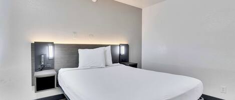 A modern hotel room with a large bed, bedside tables, and built-in lighting.