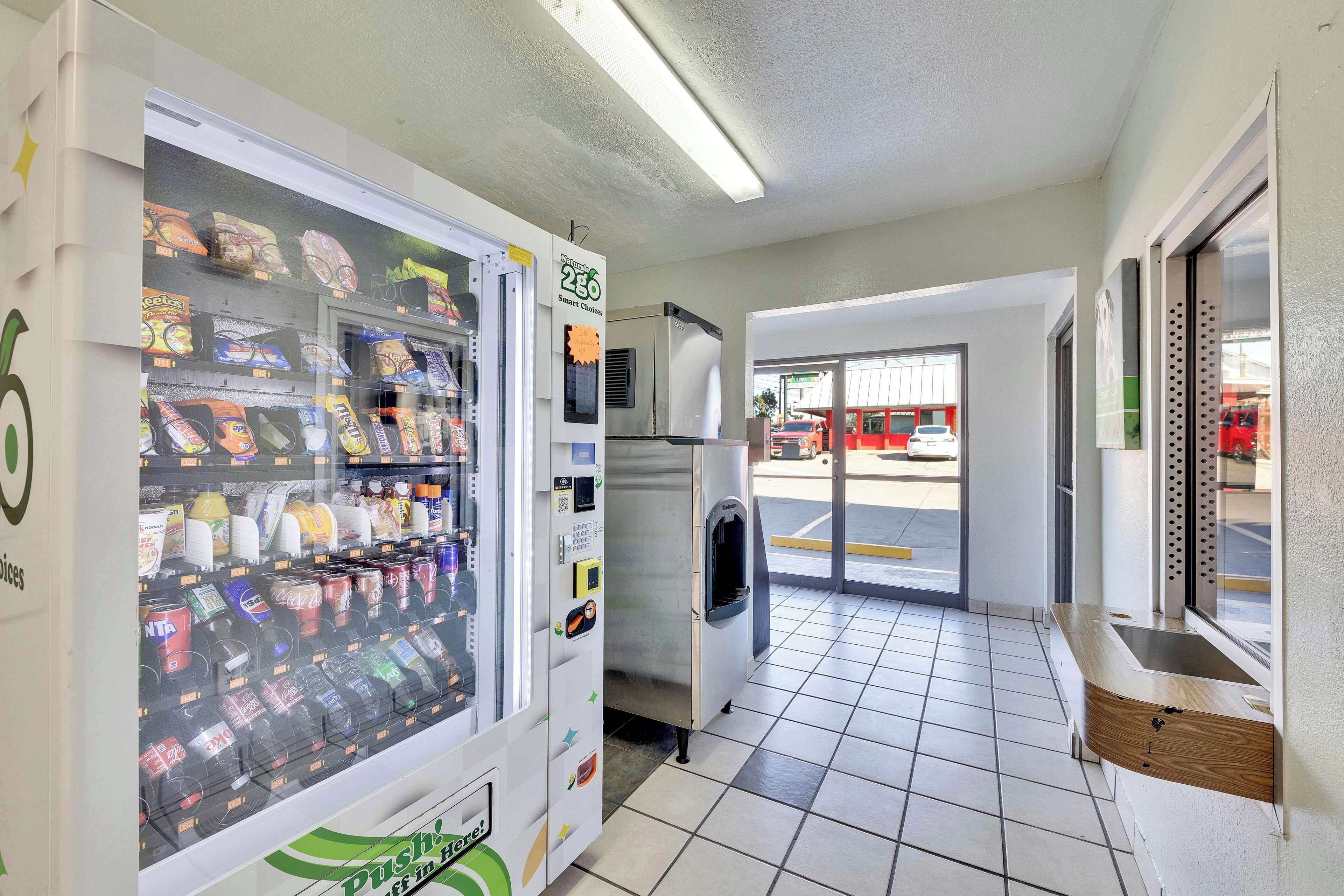 A vending machine stocked with snacks and drinks, a refrigerator, and a window with a view of the outside.